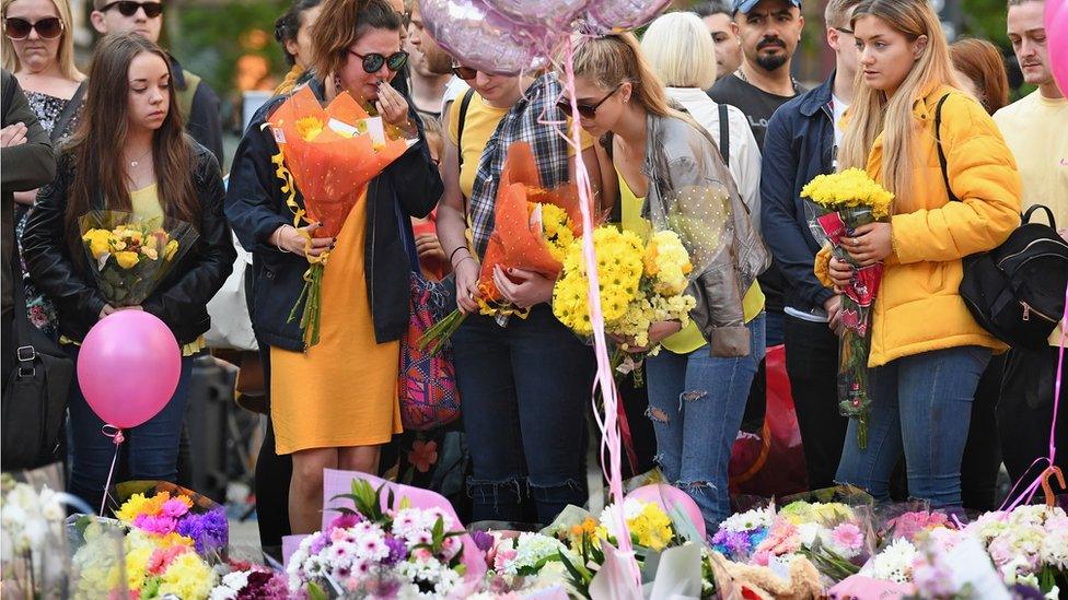 Members of the public pause to look at floral tributes and messages in St Anns Square