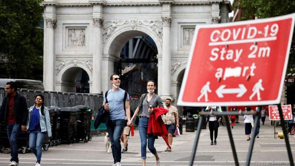 People walking past Covid-19 warning sign in Marble Arch, London