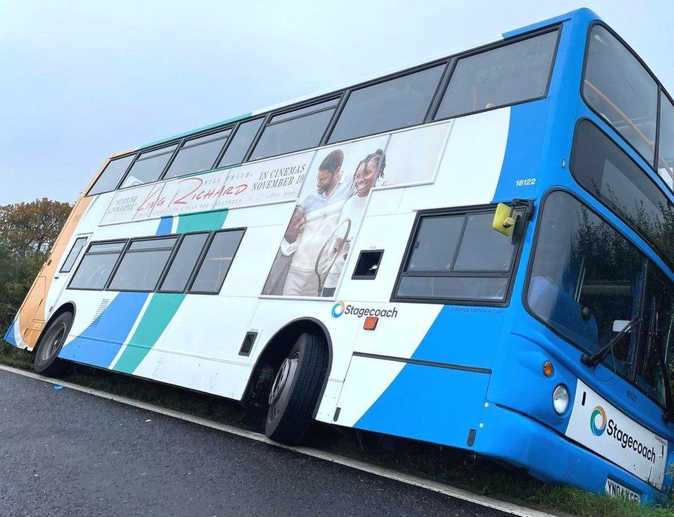 The bus leans onto a hedgerow