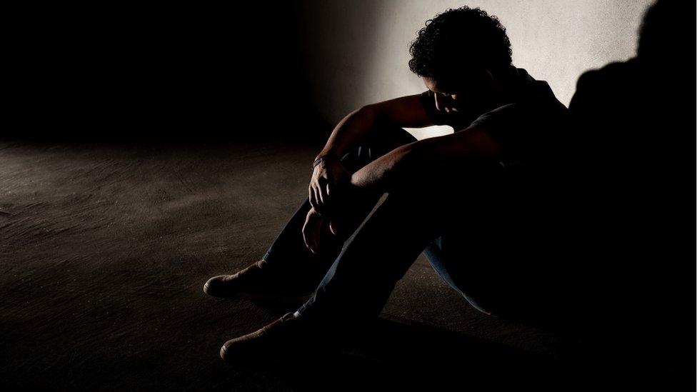 Man sitting in dark against a wall (modelled)