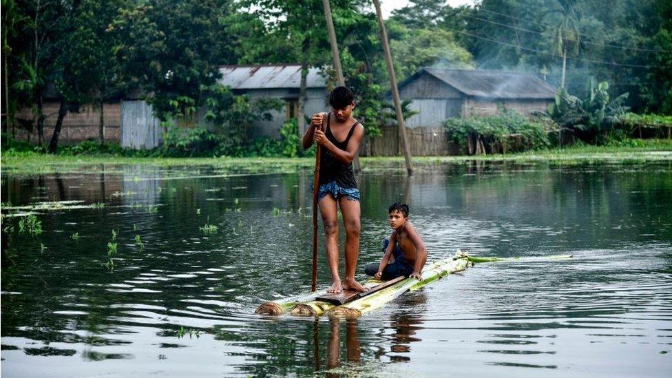 Indian children paddle a raft through floodwaters