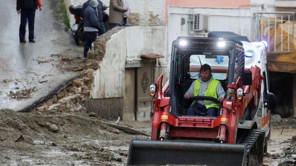 A man in a bulldozer removes mud from a street