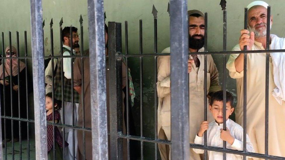 Afghans wait behind a fence to cross into Pakistan at Torkham