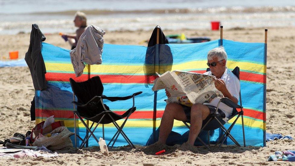 A man reading a newspaper on a UK beach