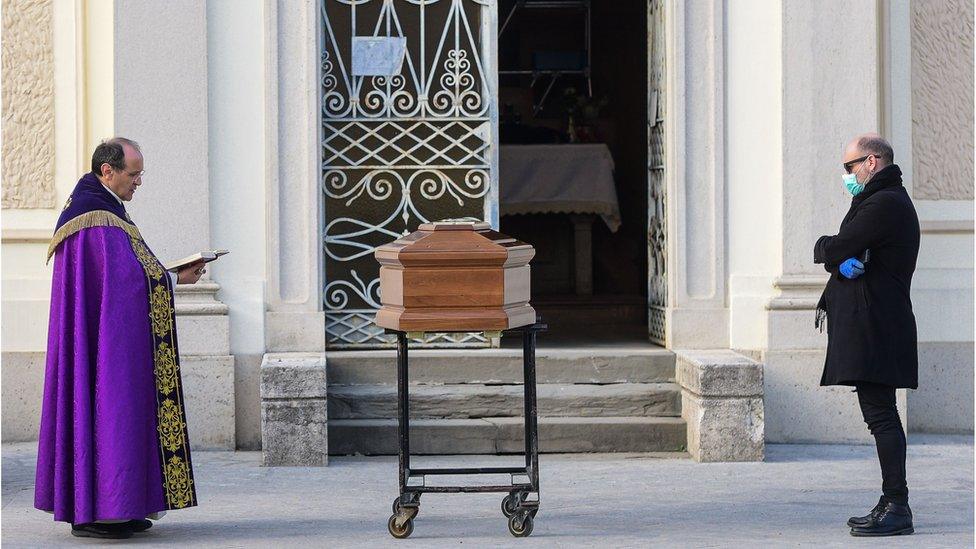 A priest minister a quick blessing to a deceased outside a church in Italy