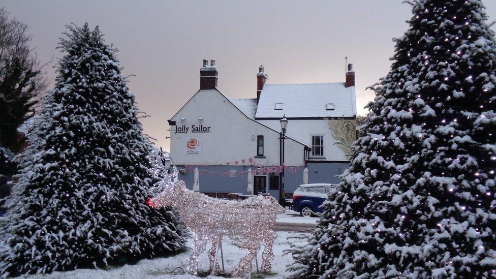 Two Christmas trees covered in a dusting of snow with an outdoor decoration of Rudolph