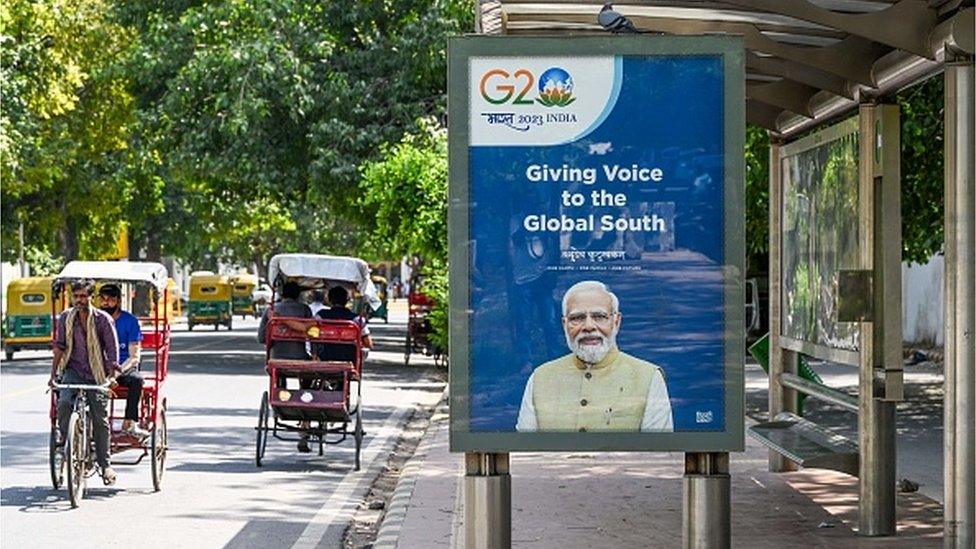 People travel on cycle rickshaws near a bus shelter displaying a G20 communication with a portrait of India's Prime Minister Narendra Modi, in New Delhi on September 4, 2023. (