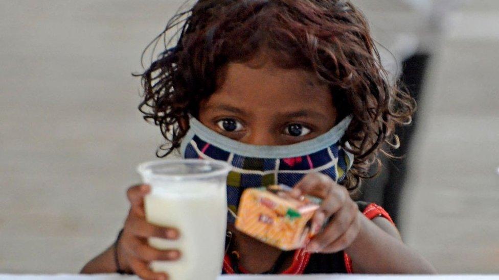 A poor child takes a glass of milk and a packet of biscuits during a free glass of milk and biscuit packet distribution organised by Kolkata police amid coronavirus emergency in Kolkata, India, 23 May, 2021. In