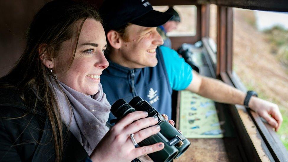 A woman with binoclaurs next to a male warden in a bird hide