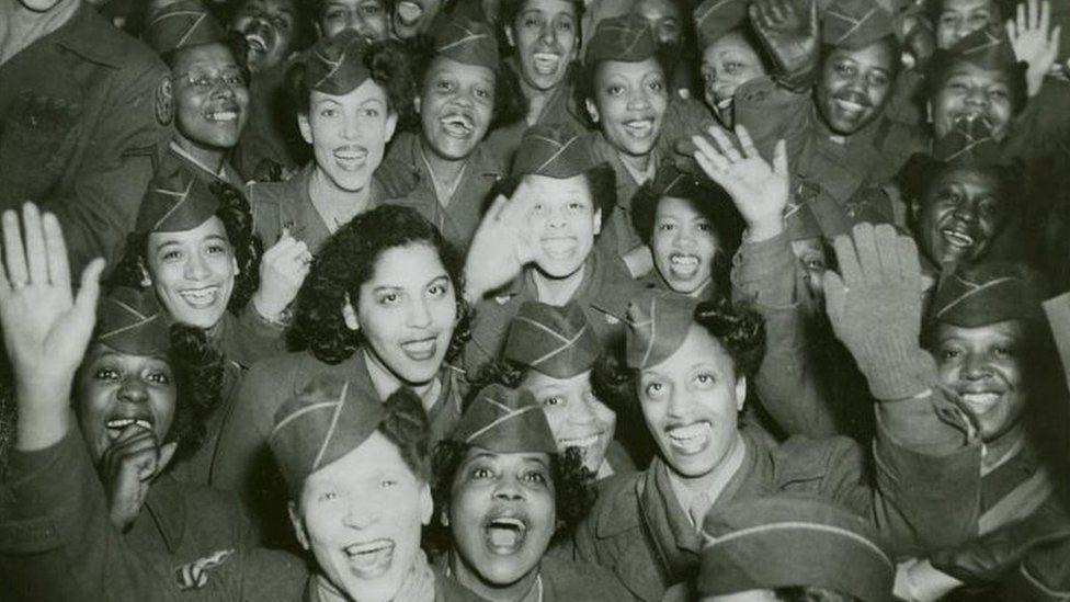 A black and white image showing a packed group least 20 women in  US World War Two uniform smiling and waving towards the camera in about 1946