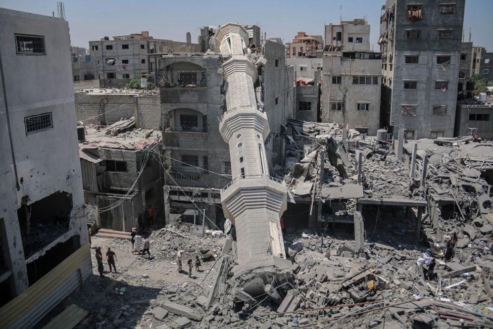 The collapsed minaret of Abdullah Azzam Mosque leans against a building after the mosque was hit by an Israeli strike in the central Gaza Strip