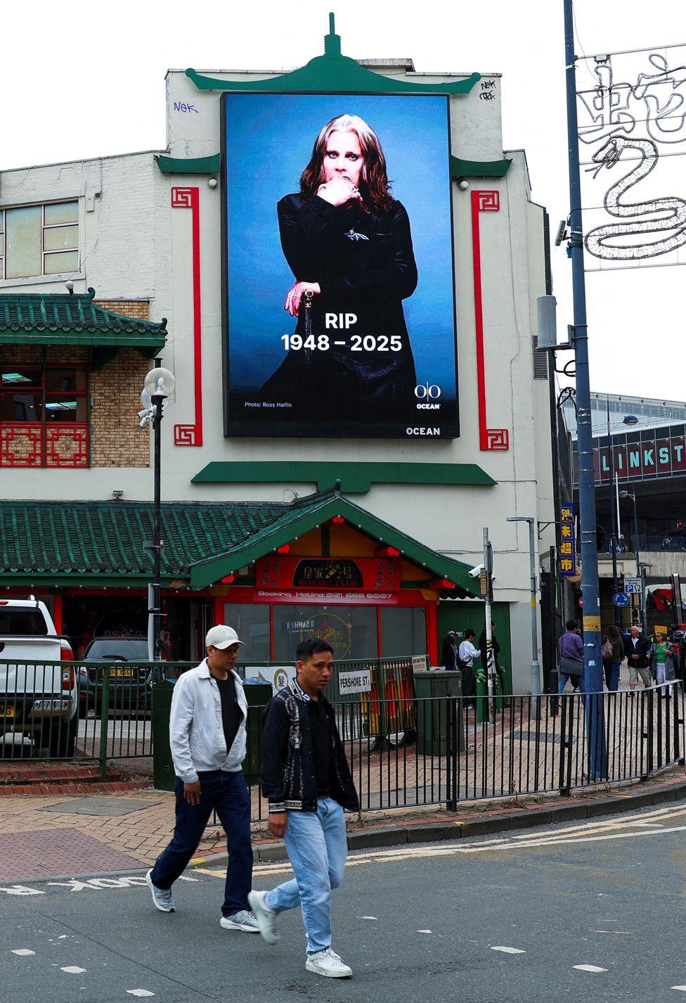 A large screen on a street, showing a picture of Ozzy and the message "RIP 1948-2025"