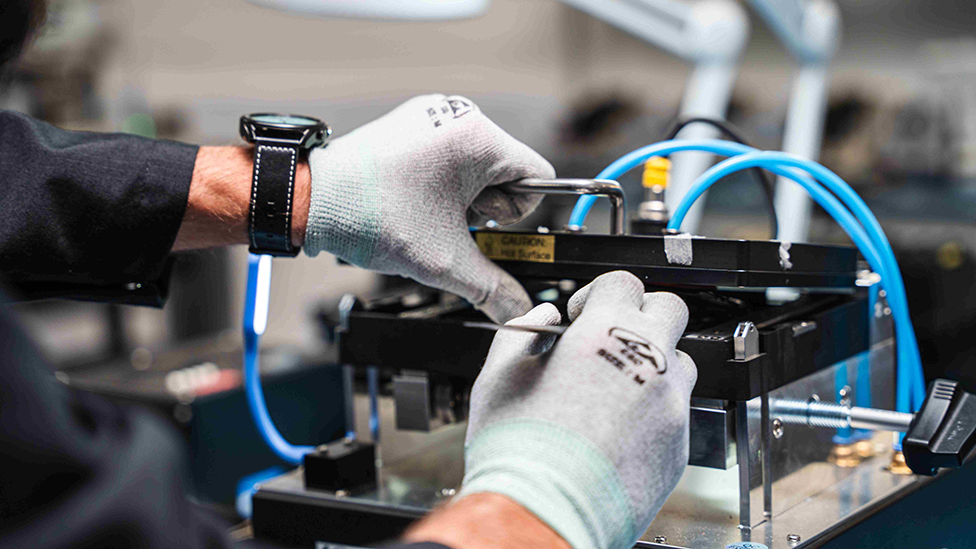 Close up of an engineer in grey gloves working at a bench on a piece of equipment.