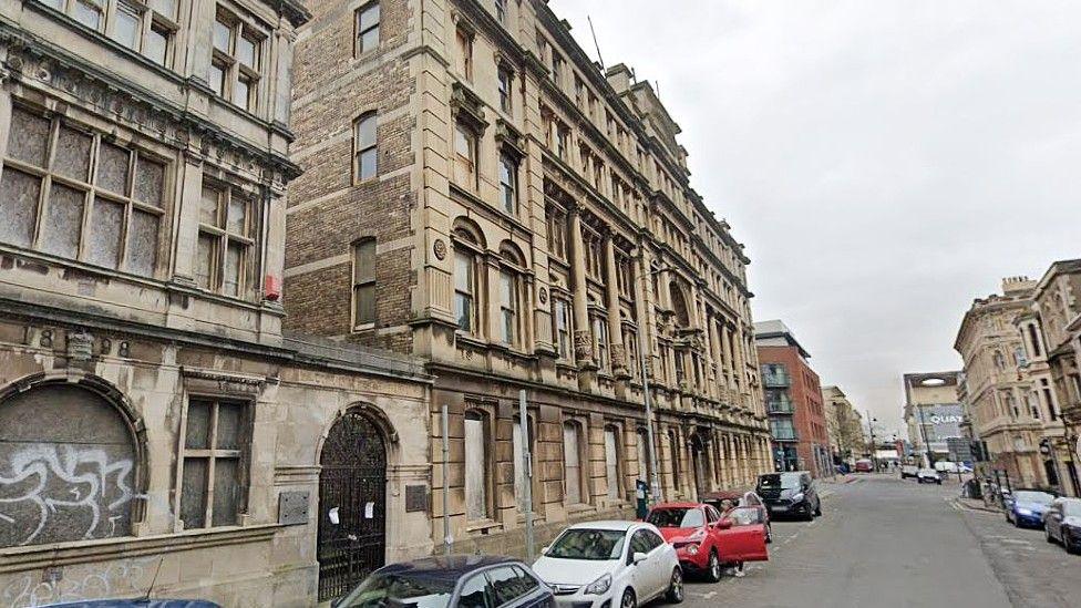 Bute Street, Cardiff, showing five-storey stone Victorian buildings, some of which are boarded up, and cars parked on the street