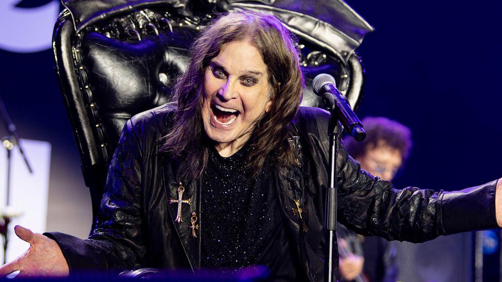 Ozzy Osbourne on stage with his arms outstretched and smiling