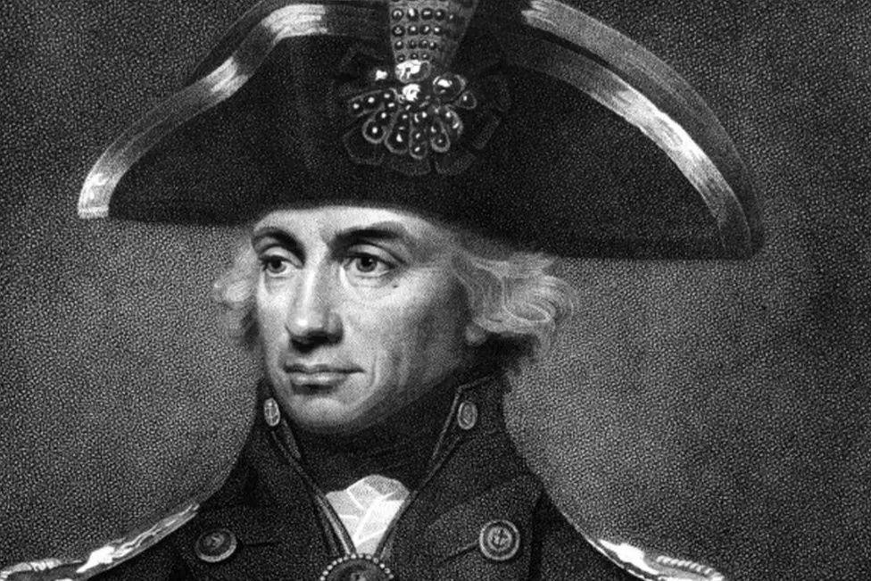 A black and white portrait of naval commander Lord Nelson. His white hair flows out of his naval hat, and his eyes are fixed slightly to the left, with a stiff, high naval collar either side of his neck.