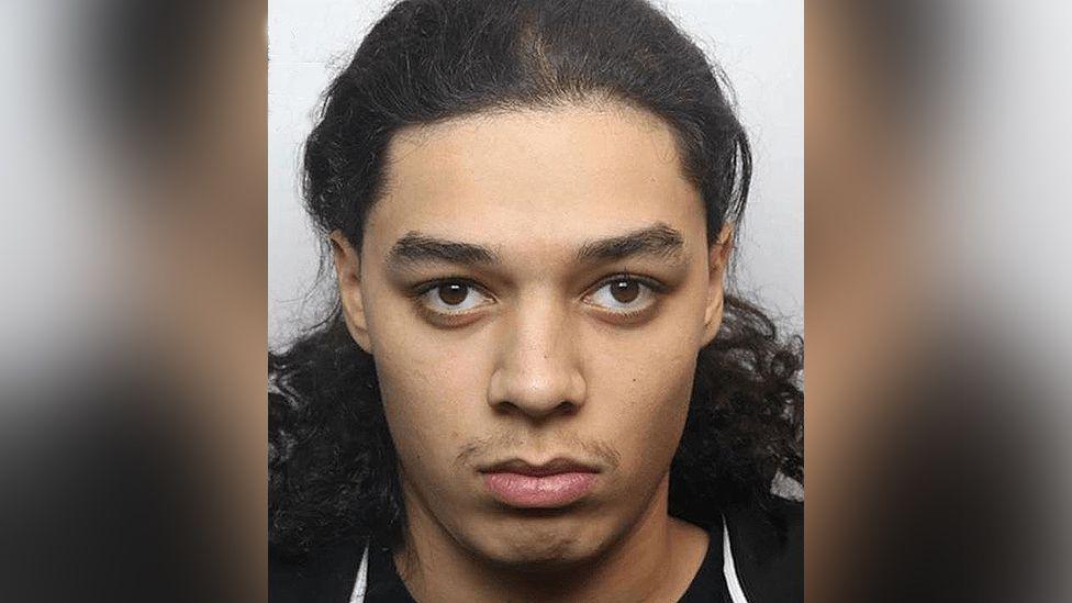 Police custody image of Harvey Bell with long dark hair and brown eyes wearing a black top.