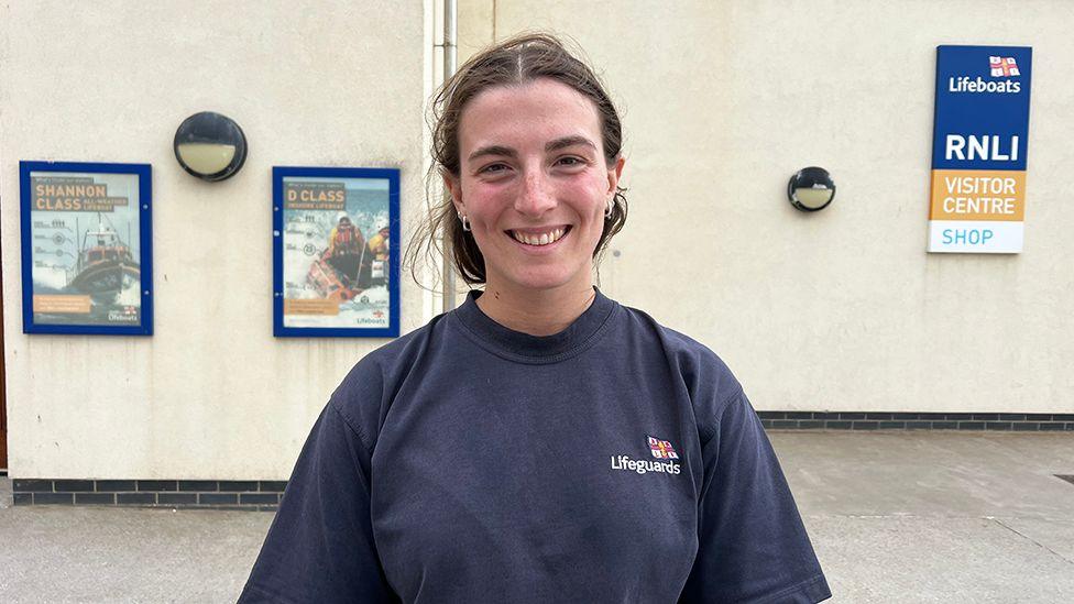 Lifeguard supervisor Rianna Manson wearing a blue RNLI sweatshirt standing in front of the RNLI lifeboat station in Bridlington