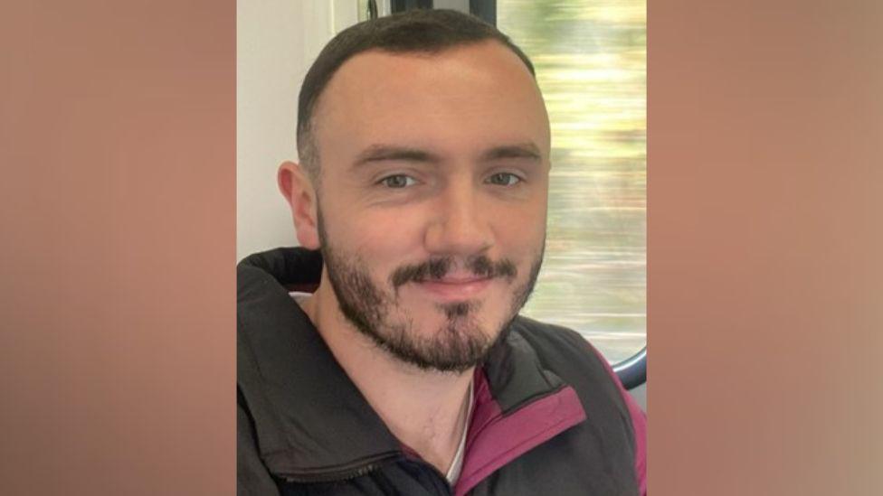 A close up picture of a man who is smiling and has short black hair and a beard. 