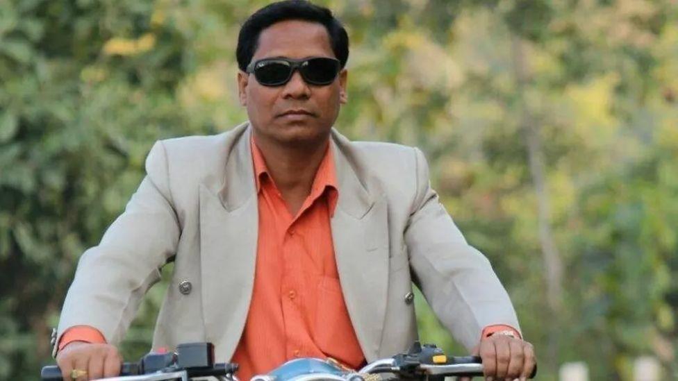 The image is of Punjilal Meher wearing a beige suit with an orange shirt on a motorbike. He was found guilty of murder, attempted murder, and use of explosives.