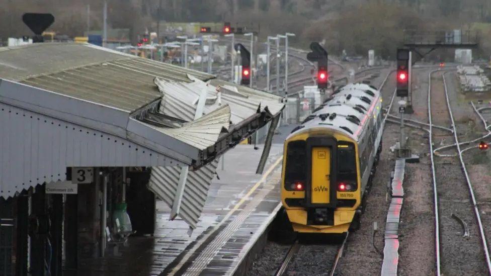 A train pulls into a railway station platform where the roof is damaged. Corrugated iron is hanging down towards the platform. 