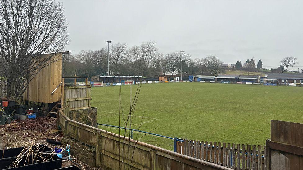 A view from the garden shows the view of the football pitch with the  wooden stand to the left