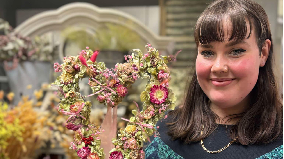 Charlotte holding her flower wreath whilst looking at the camera. The wreath is shaped in a heart. 