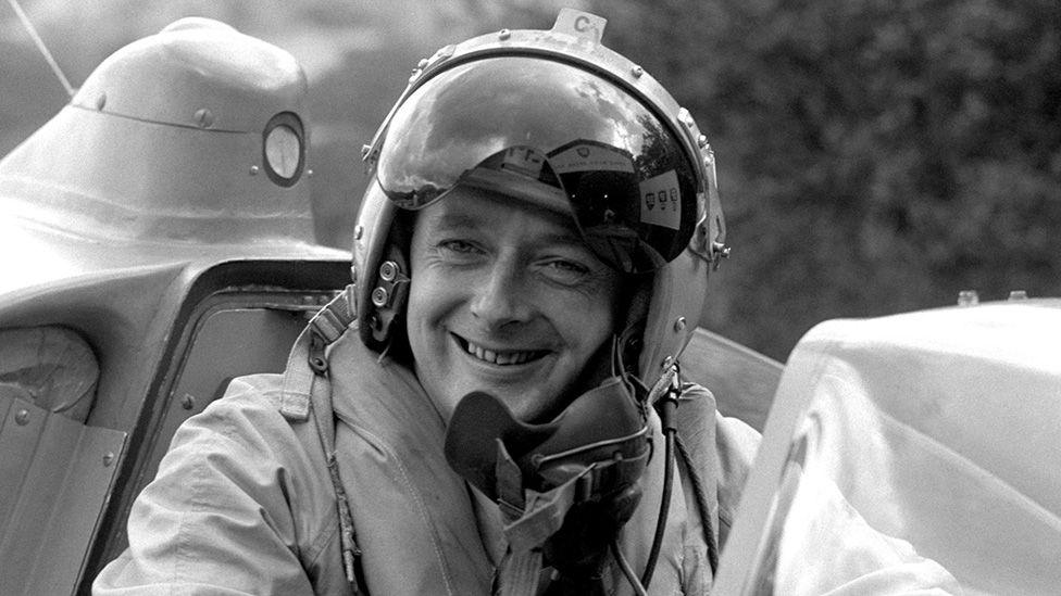 Black and white file photo from 1958 of Donald Campbell in the cockpit of his jet-powered hydroplane 'Bluebird' at Lake Coniston, smiling at the camera and wearing a helmet