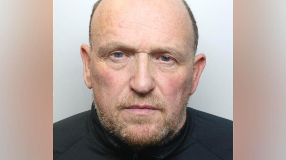 Martin has a brown greying beard, and cropped brown greyign hair and is wearing a black shirt.