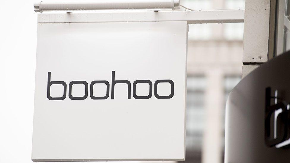 Clos-up of a square, white hanging sign on a shop saying "boohoo" in black text