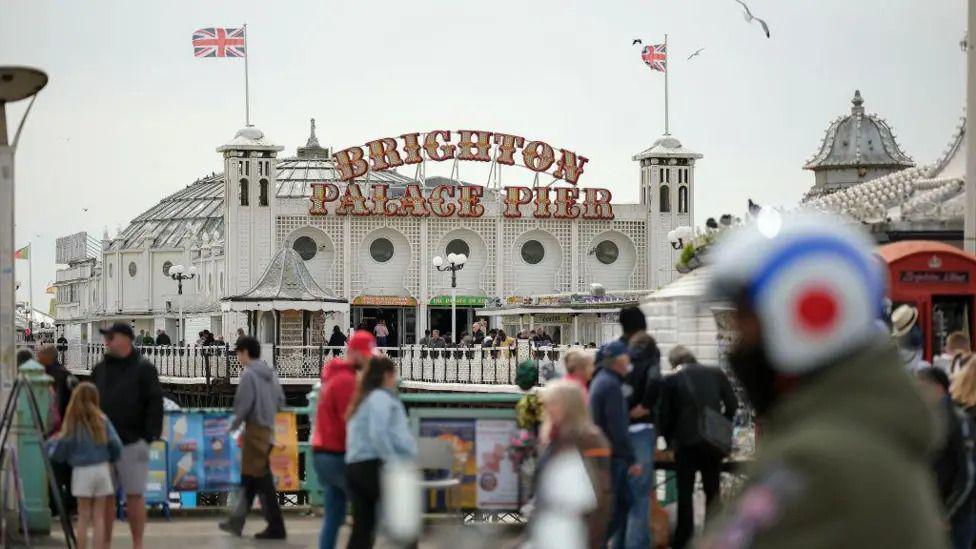 Crowds of people in foreground with the pavilion on Brighton Palace Pier behind them.