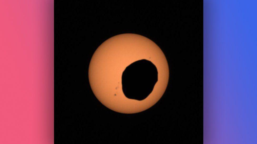 A photo of Phobos silhouetted against the Sun.