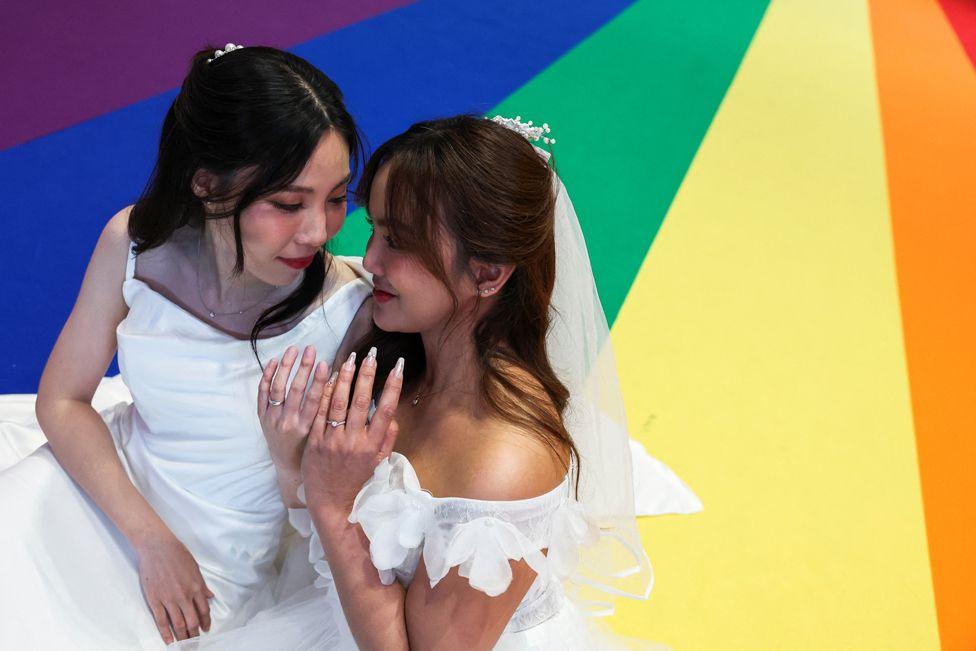 Natnicha Somparn, 31, and Sorsomrudee Thippayatum, 32, pose for a picture as they celebrate after receiving official marriage certificates, as the country's marriage equality bill comes into effect following a royal endorsement in Bangkok, Thailand, January 23, 2025. The are wearing white dresses and are standing on a rainbow coloured painted floor.