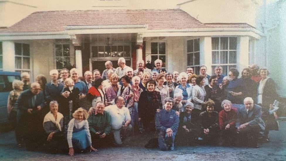 A group of people stood outside a hotel looking towards the camera 