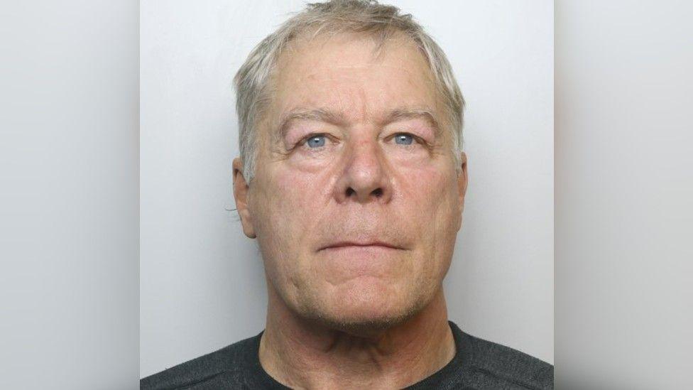 Headshot of a man with grey hair and blue eyes. He is wearing a black shirt.