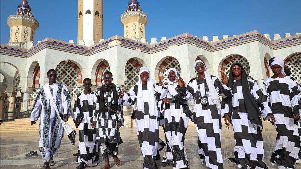 A line of male and female Baye Fall members dressed in flowing black and white chequered robes are pictured in front of Touba's Grande Mosque