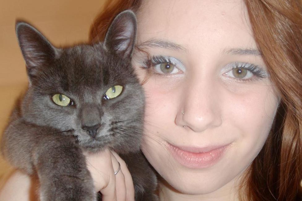 Alice, a woman with long blonde hair, poses for a photo while holding a grey cat
