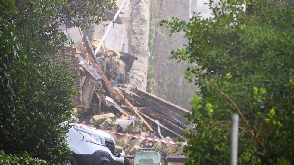 Front of white van seen with tape across a drive and a large pile of stone rubble  