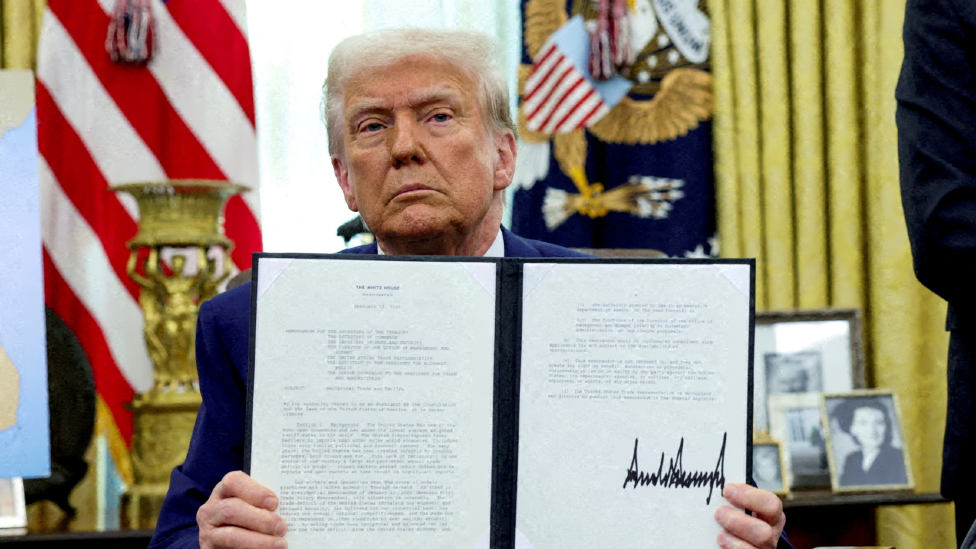 President Trump in the Oval Office holding up a declaration that he has signed. 