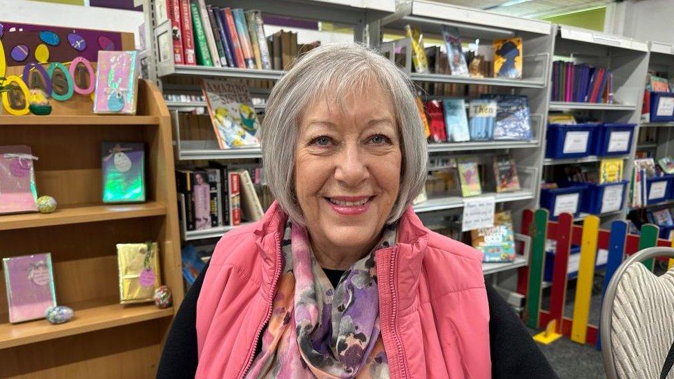 Woman wearing a pink top standing in front of shelves of books