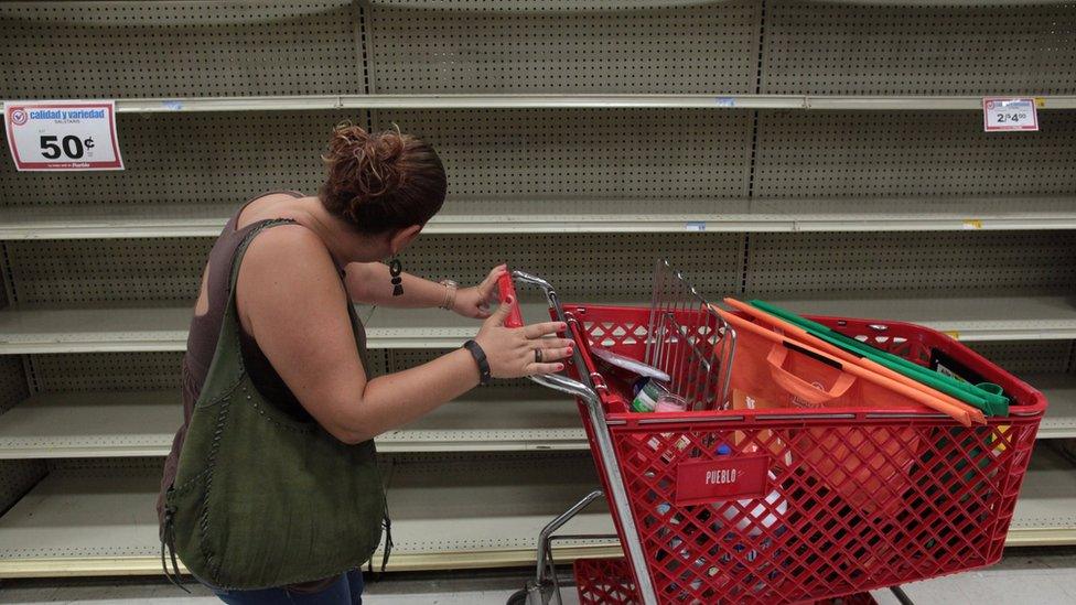 A woman looks at empty shelves that are normally filled with bottles of water in a supermarket in San Juan, in Puerto Rico