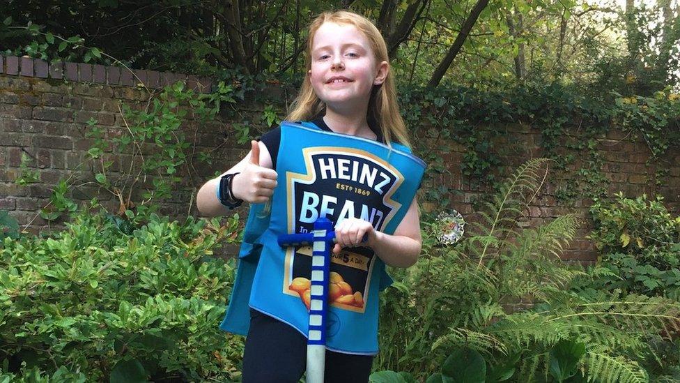 Luna on a pogo stick. She is wearing a Heinz Beans costume and has a thumb up. She is smiling at the camera.