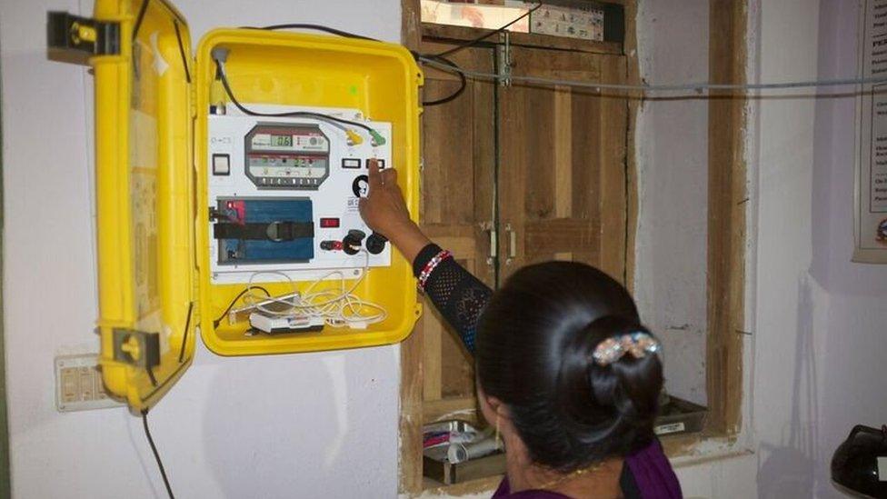 Midwife Hima Shirish switches on yellow suitcase fixed to wall housing mobile solar power station