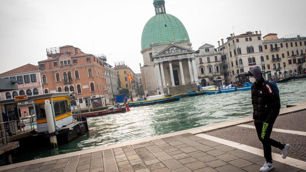 Man wears face mask walking next to a canal in Venice