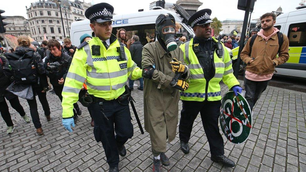 A protester wearing a gasmask and boiler suit with police