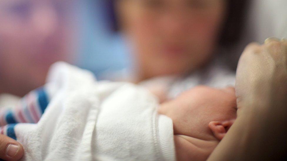 Generic close-up shot of a newborn baby with parents blurred in the background