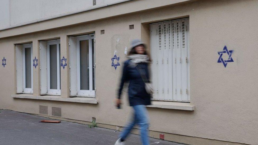 A woman walks along a building whose facade is covered with Stars of David in Paris