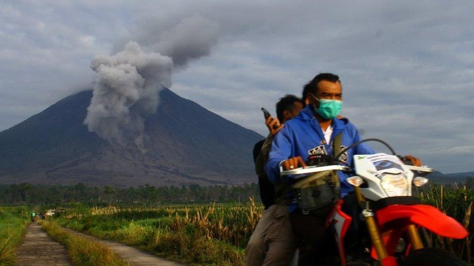 Villagers ride a motorcycle as Mount Semeru volcano spews ash and smoke in Tuesday image