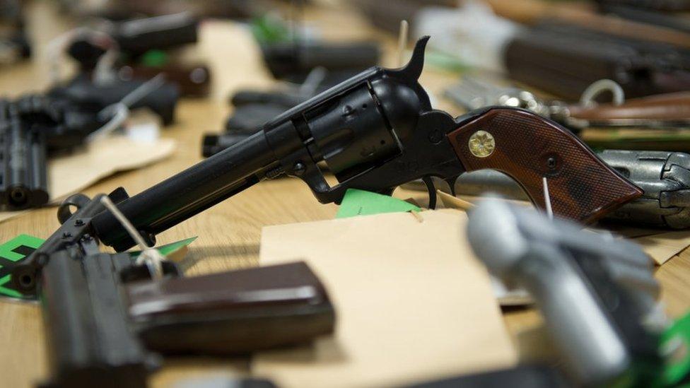 Pistol in an upright position on a table surrounded by other firearms