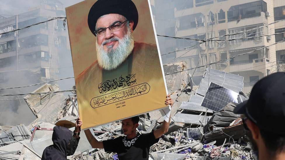 A Hezbollah supporter holds a placard with Hezbollah leader Hassan Nasrallah next to the rubble of a completely destroyed building in Dahieh, a southern suburb controlled by Hezbollah, Beirut, Lebanon, 2 October 2024